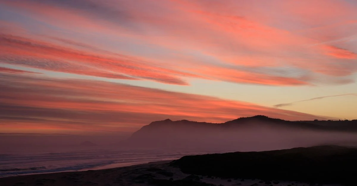 A breathtaking sunset over a misty coastal landscape with vivid hues and clouds.