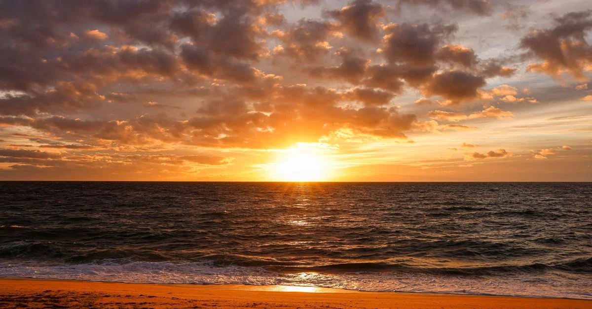 Beautiful sunset over the ocean with a sandy beach and dramatic sky.