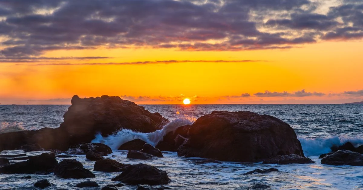 Breathtaking sunset over a rocky coastline, capturing vibrant colors and dynamic waves.