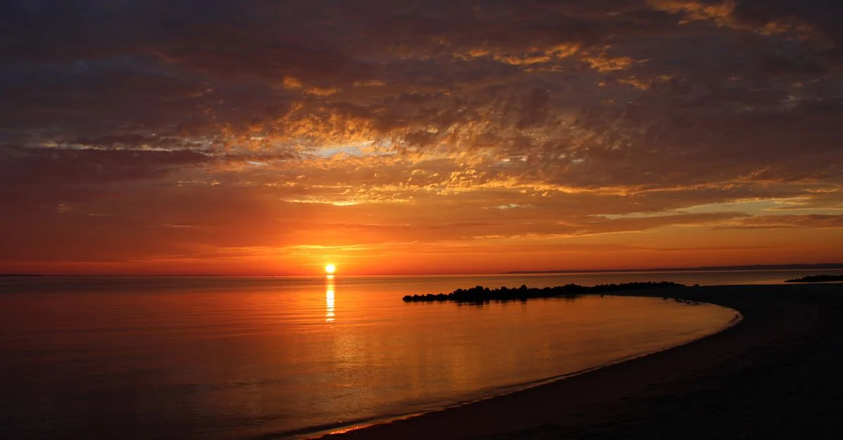 Dramatic sunset over a tranquil beach with vibrant reflections on calm water.