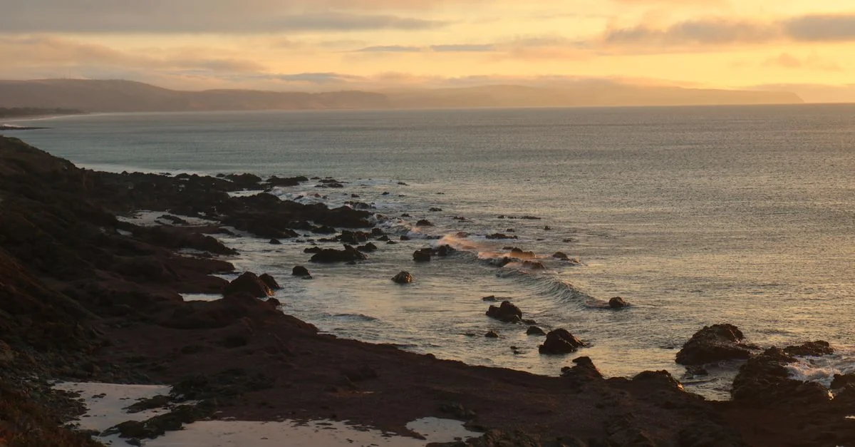 Beautiful sunset over a rocky shore with waves gently hitting the coast, capturing a serene and natural seascape.