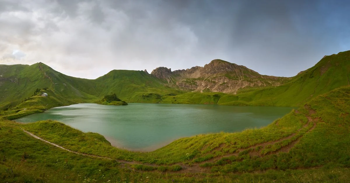 Panoramic view of a serene alpine lake surrounded by lush green hills in Bad Hindelang, Bavaria, Germany.