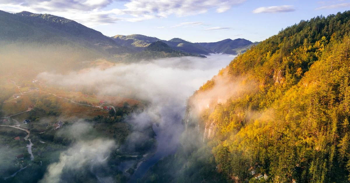 A stunning aerial view of a misty mountain landscape with autumn foliage under a clear morning sky.